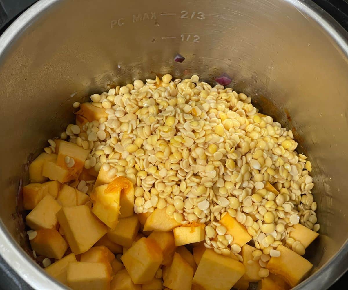 An instant pot is with pumpkin cubes and lentils.