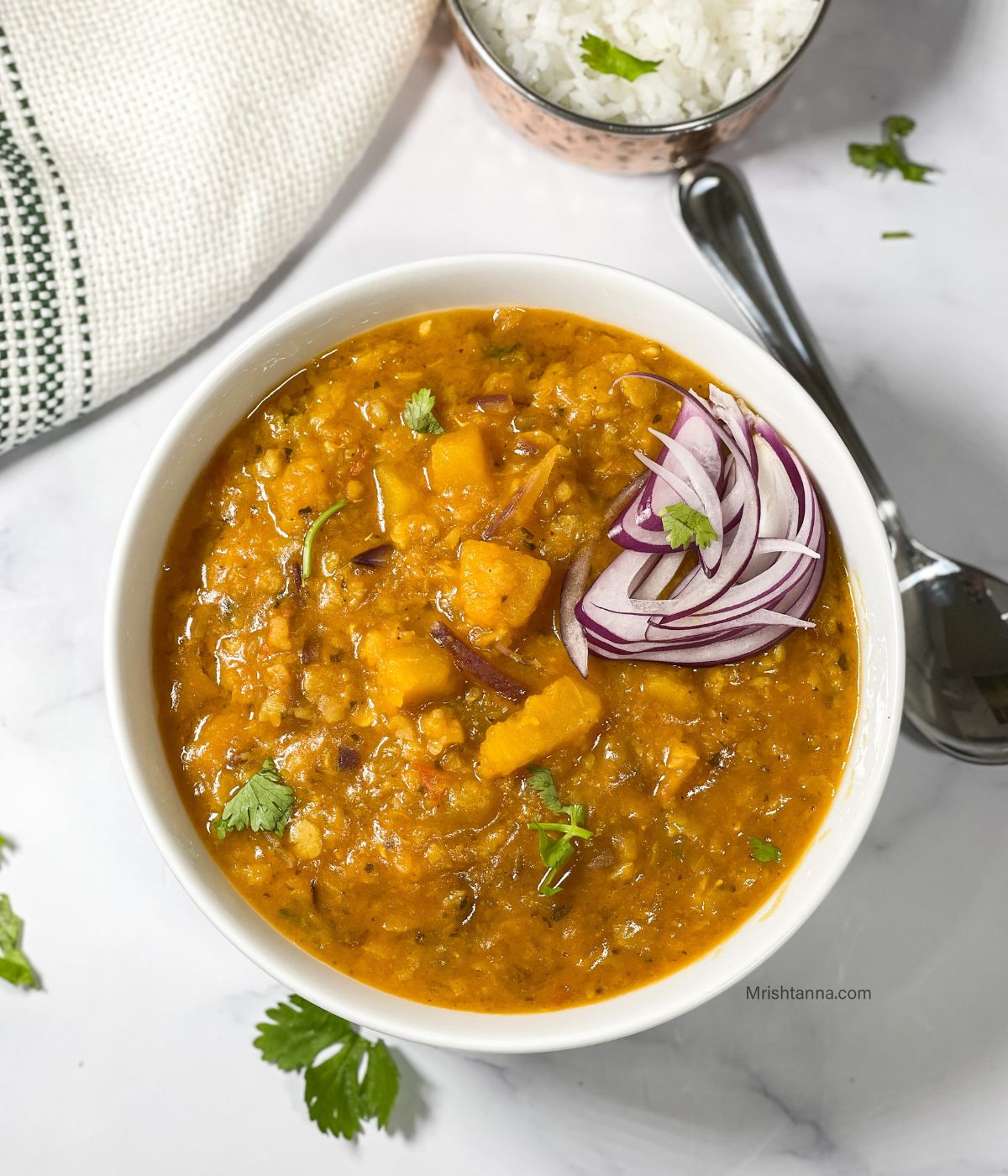 A bowl of pumpkin dal and it is topped with raw onions and cilantro.