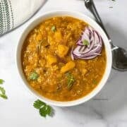 A bowl of pumpkin dal is on the table with a spoon by the side.