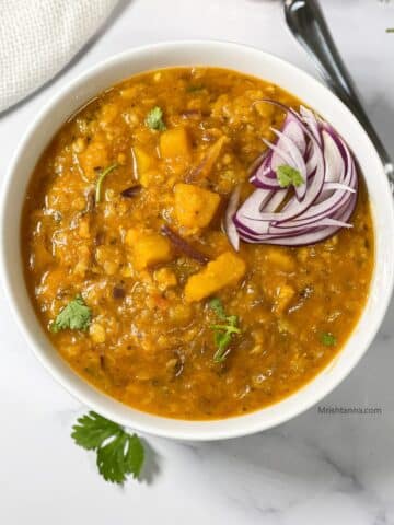 A bowl of pumpkin dal is on the table with a spoon by the side.