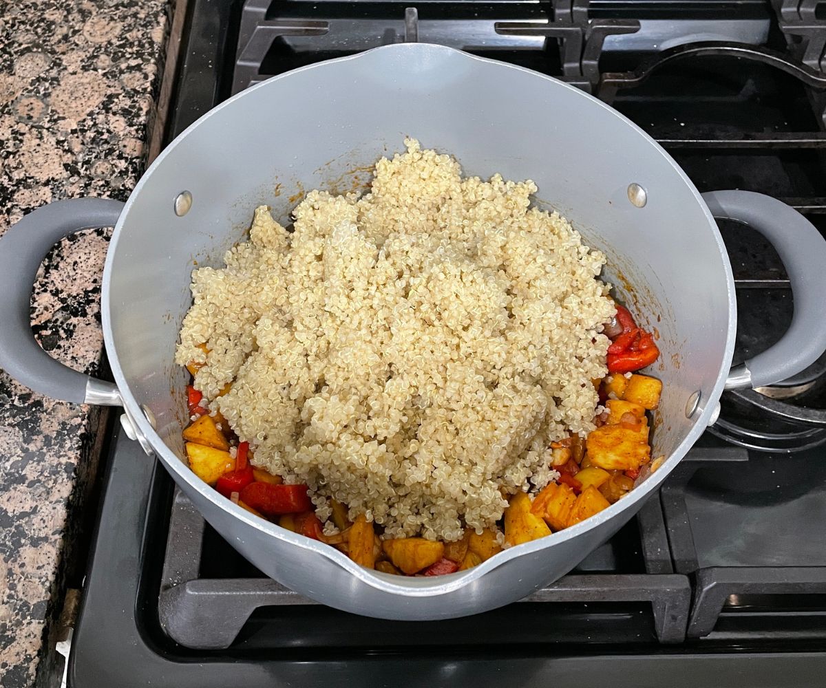 A pot is with spices, pineapple and quinoa over the stove top.