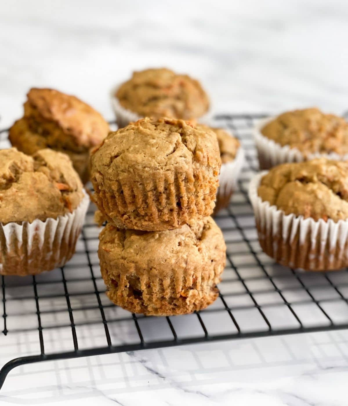 Stacked banana carrot muffins are on the wire rack.