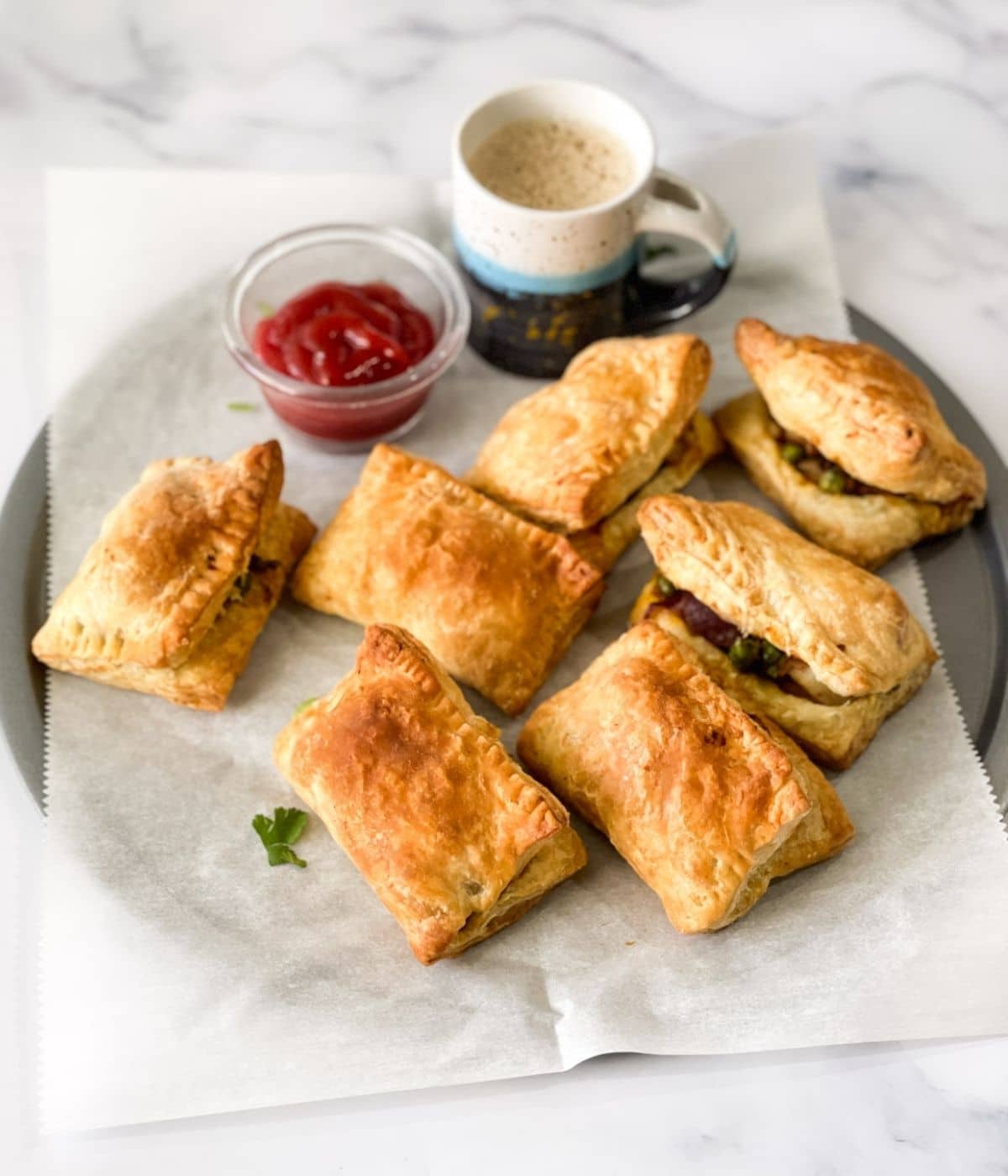 A tray of curry puff's are on the table along with chai and sauce.