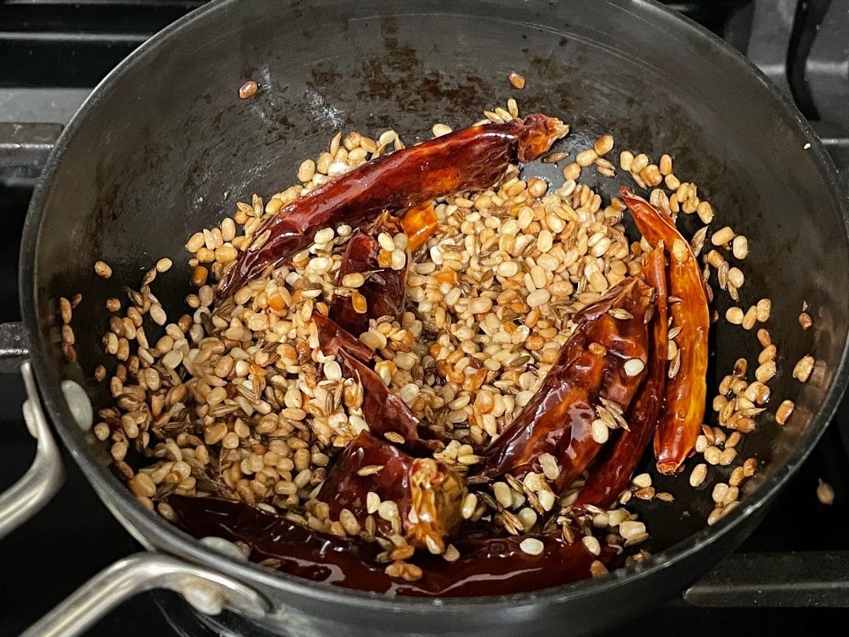 A small pan is with spices and chilies over the heat