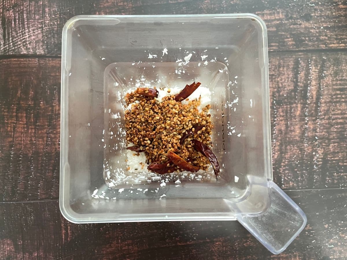 A blender is with sauteed spices and grated coconuts on the table