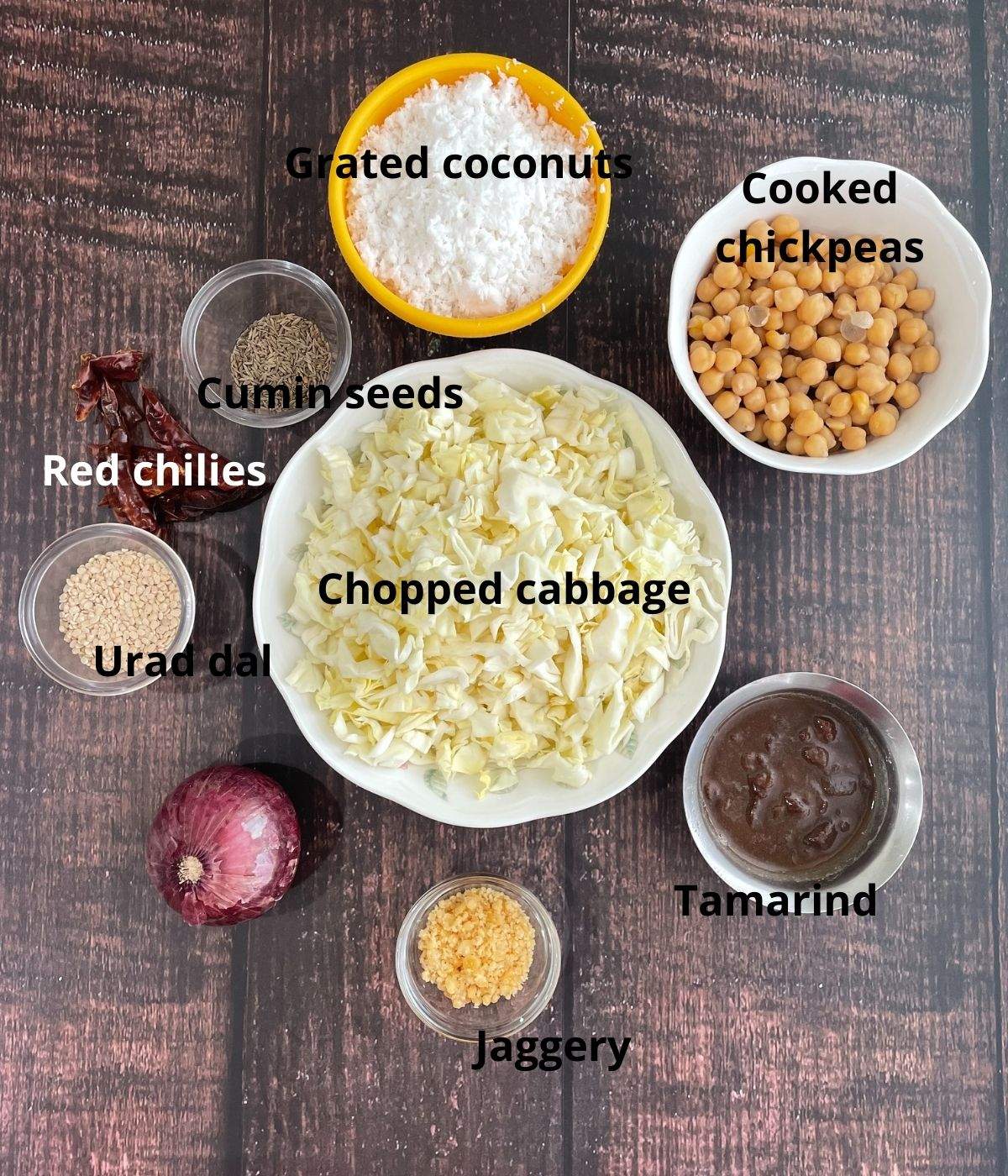 A brown surface is filled with gassi ingredients like cabbage, onion, coconuts and spices