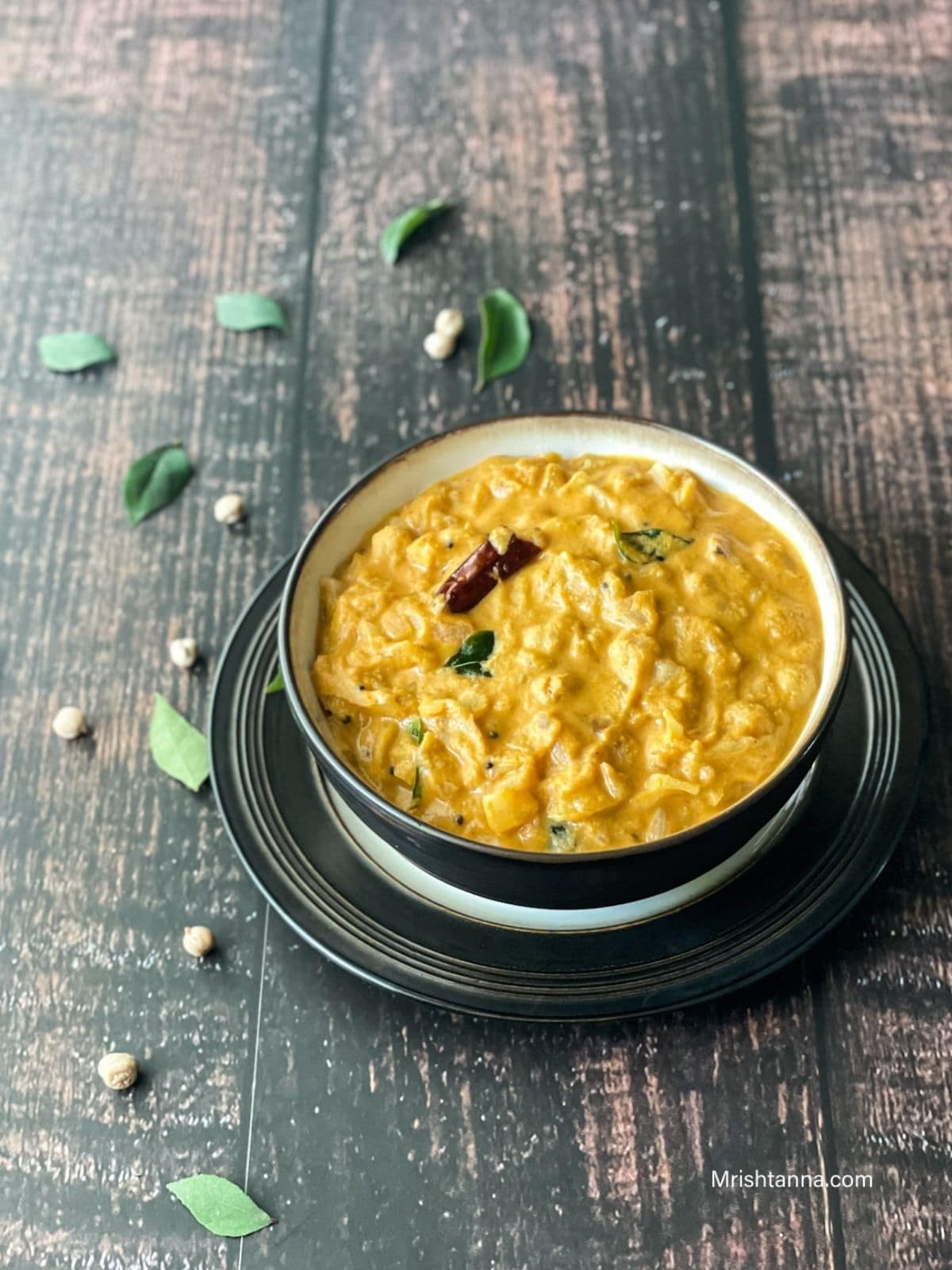 A black bowl is filled with cabbage and chickpeas curry on the table