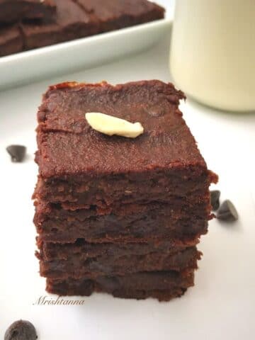 vegan brownies are stacked on the white surface along with jar of milk