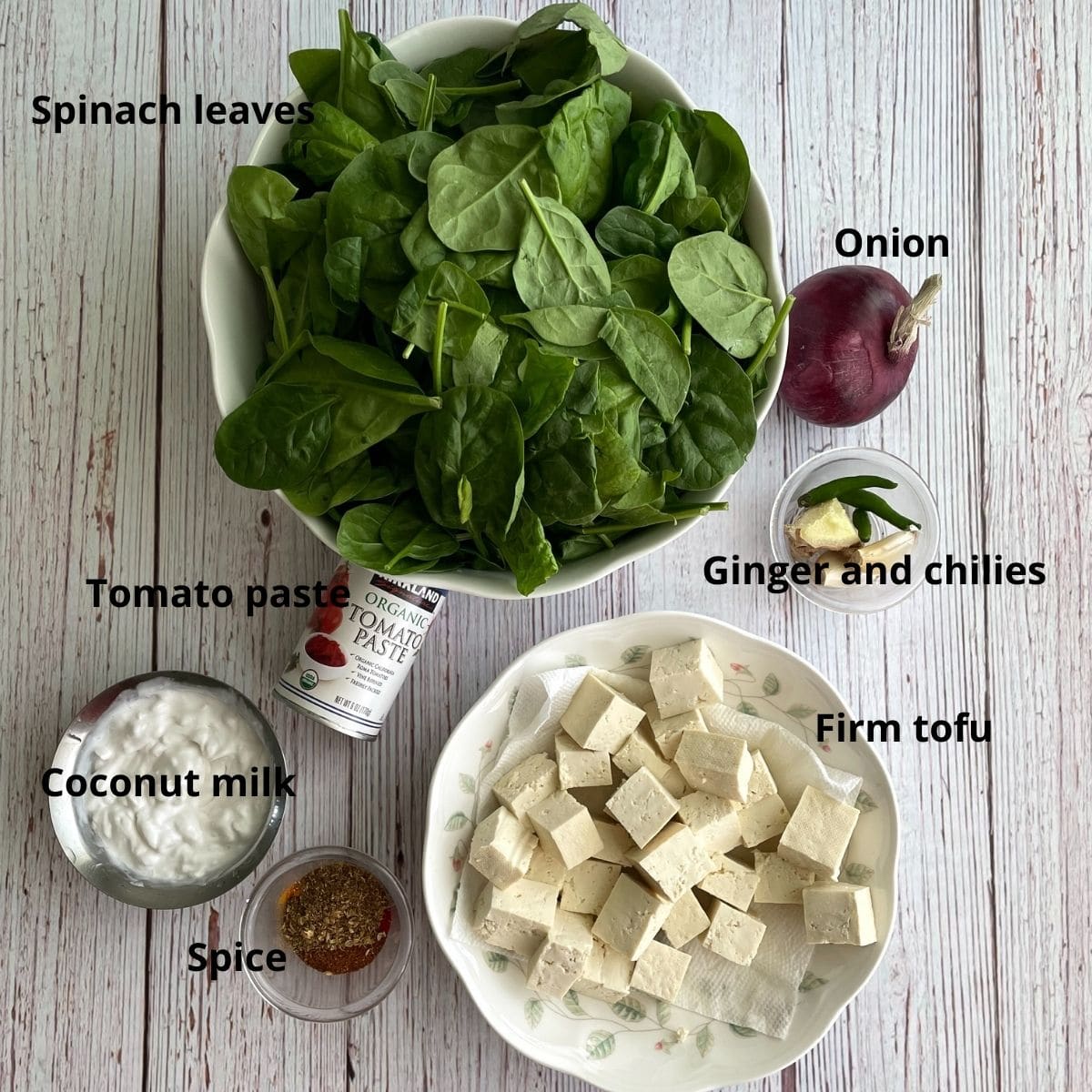 Spinach leaves, firm tofu, spices, onion and tomato paste are on the table for curry