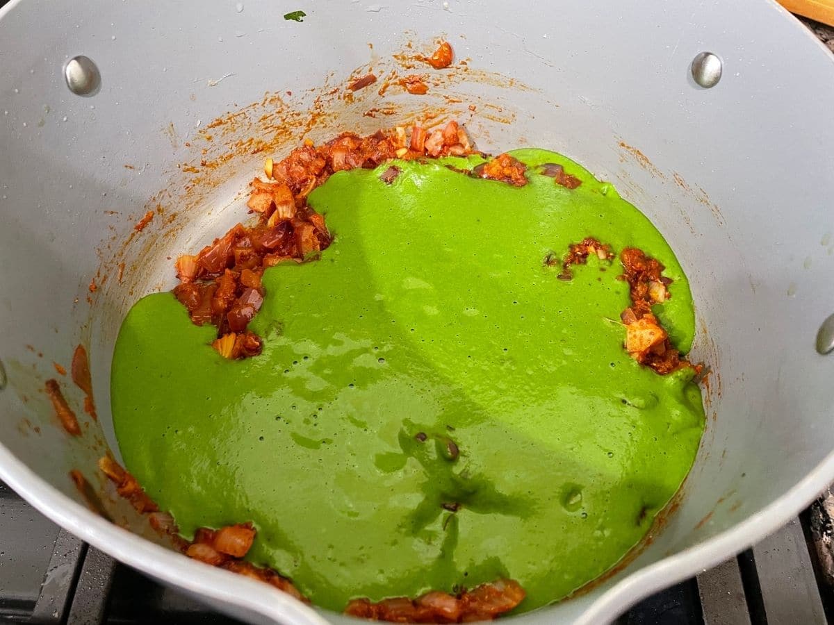 A pan is with spinach puree and spices over the heat.