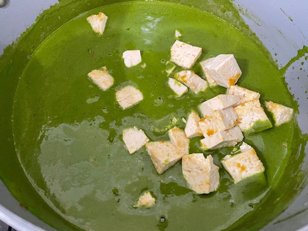 A pot is filled with palak tofu curry over the heat
