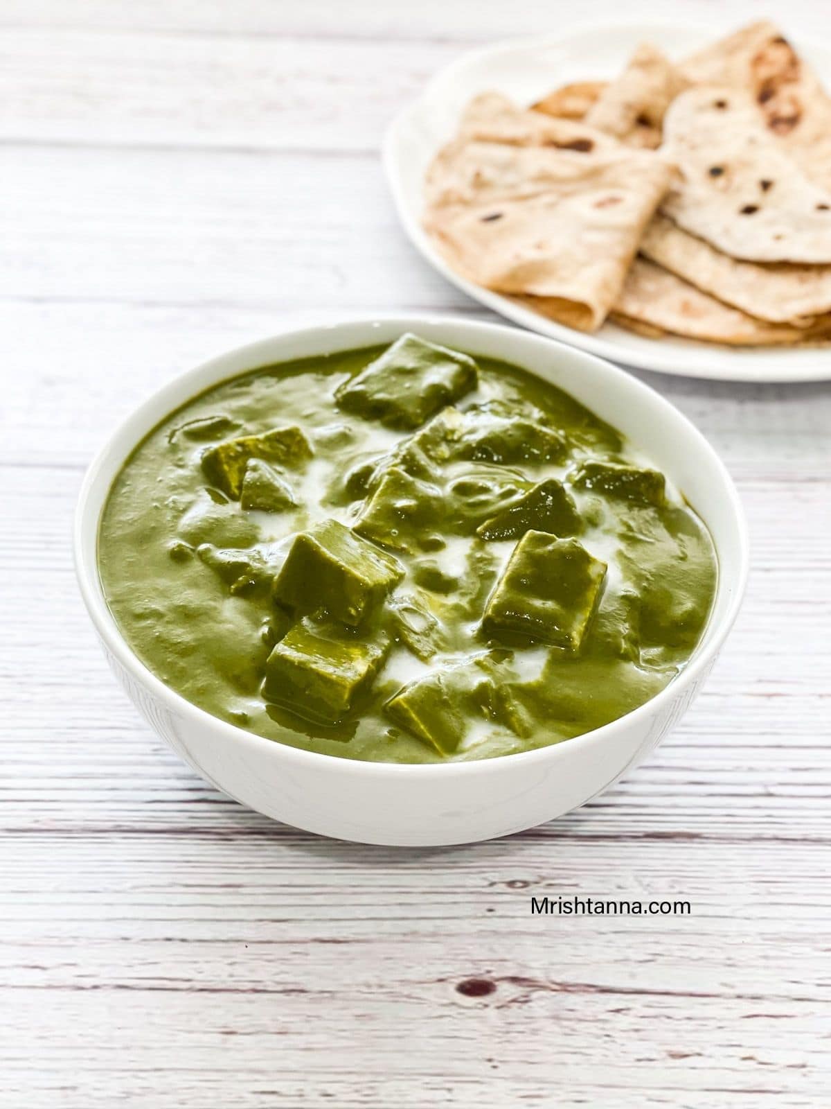 A bowl of palak tofu is on the table topped with coconut cream