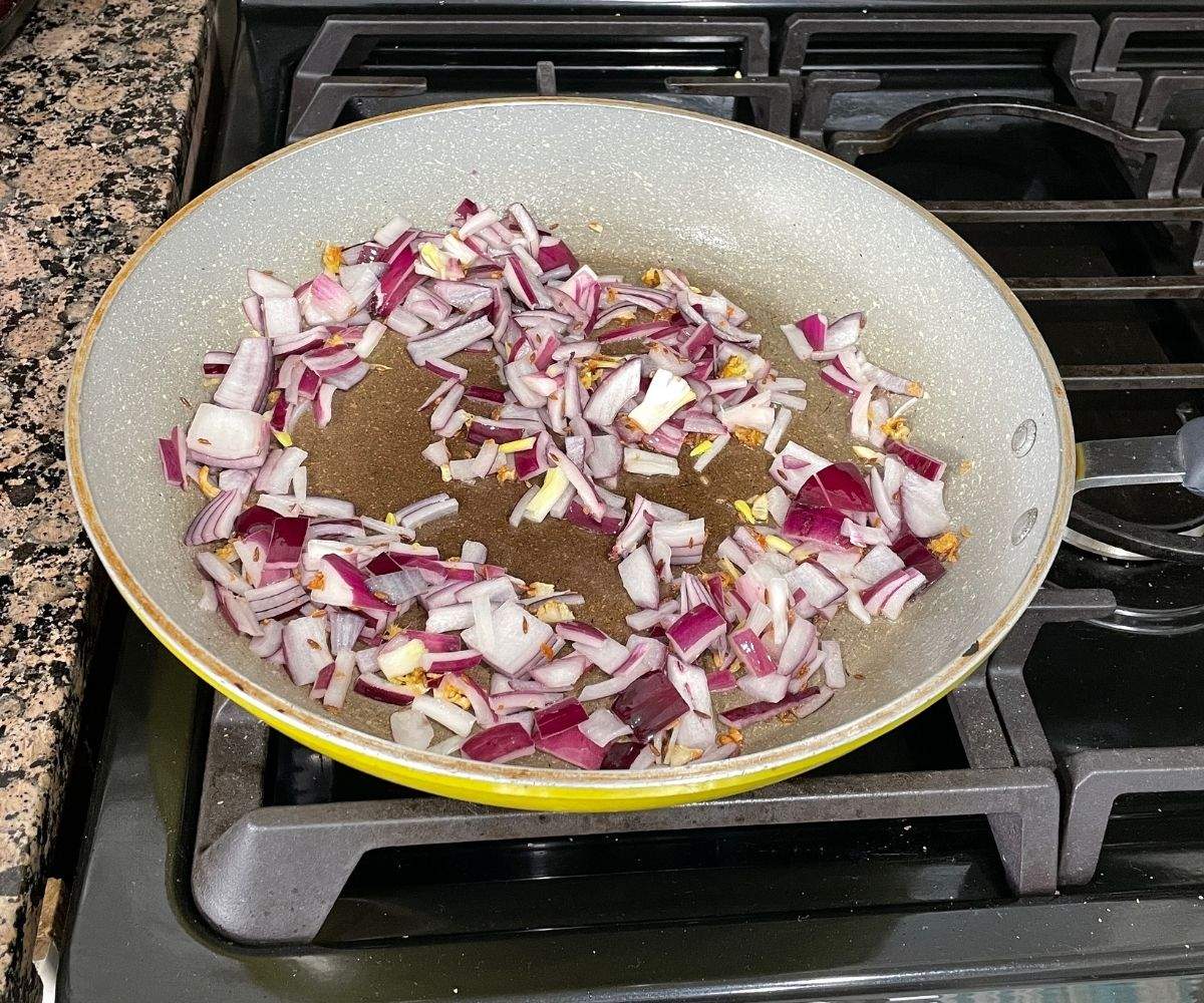 A pan is with spices and onions over the flame.