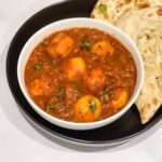 A bowl of dum aloo curry is on the table with naan.