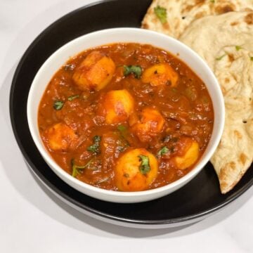 A bowl of dum aloo curry is on the table with naan.