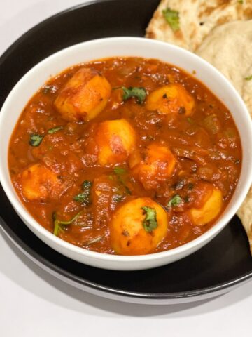 A bowl of dum aloo curry is on the table with naan.