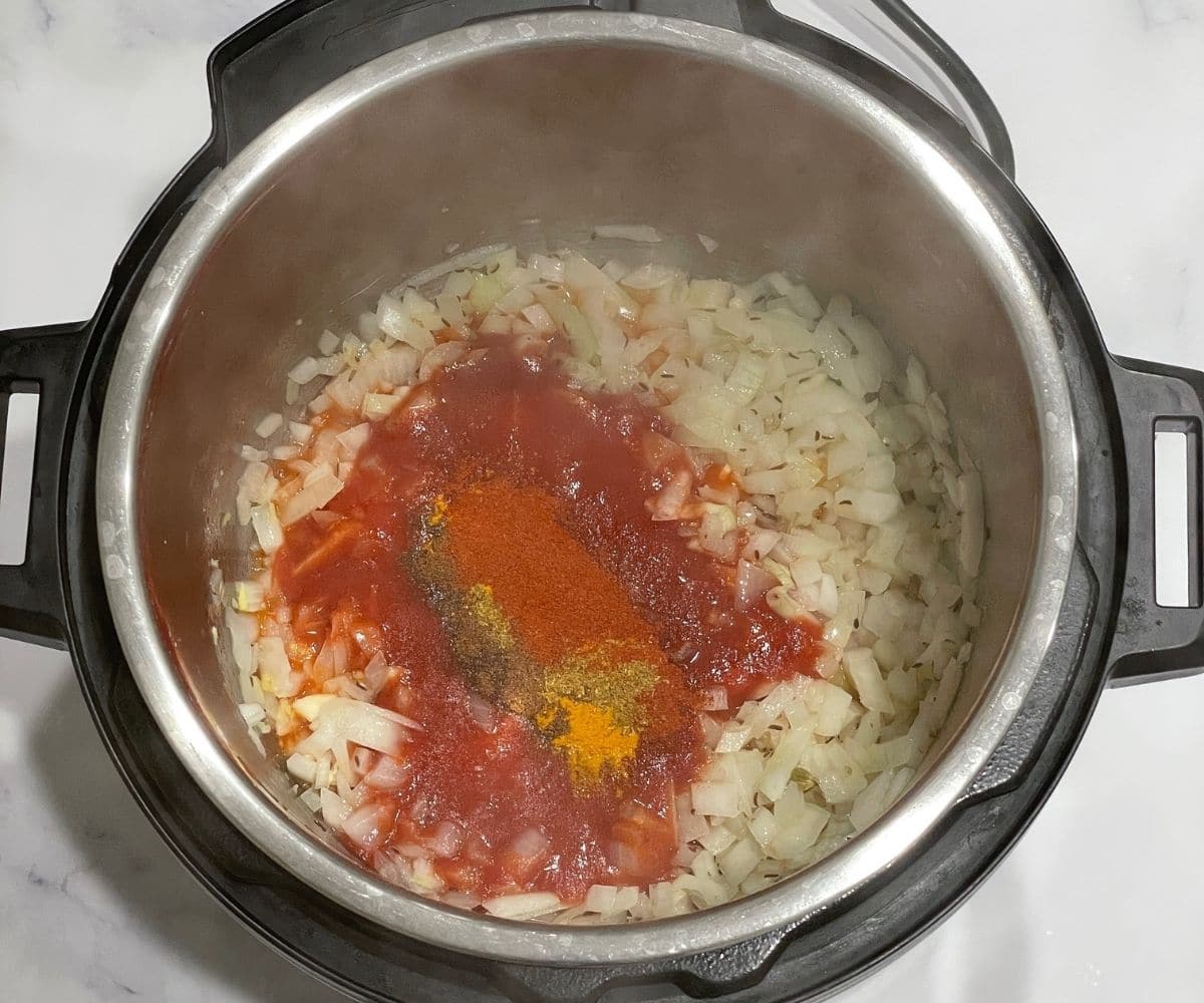 An instant pot is with tomato puree and spices to make dum aloo.