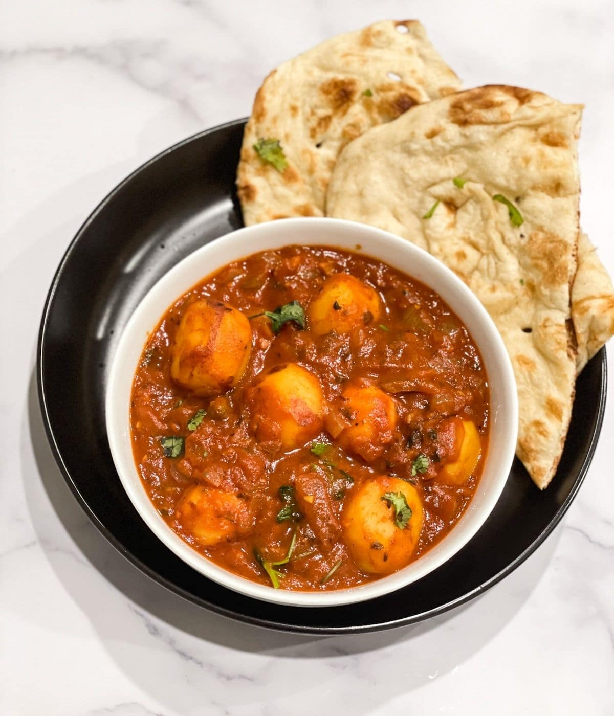 Instant pot dum aloo is poured on the bowl along with naan.