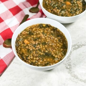 A bowl is with kale lentil soup and placed on the flat white surface