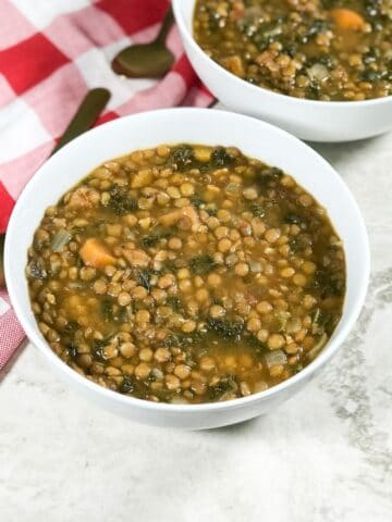 A bowl is with kale lentil soup and placed on the flat white surface