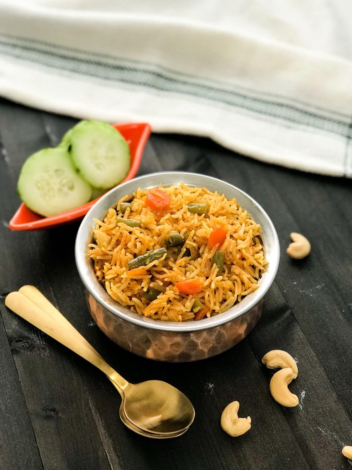 A copper pot is filled with vegetable rice and topped with cashew nuts