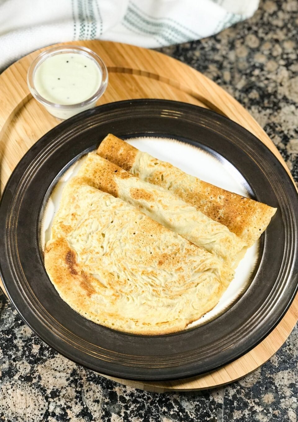 A plate of oats dosa and bowl of chutney is on the serving tray