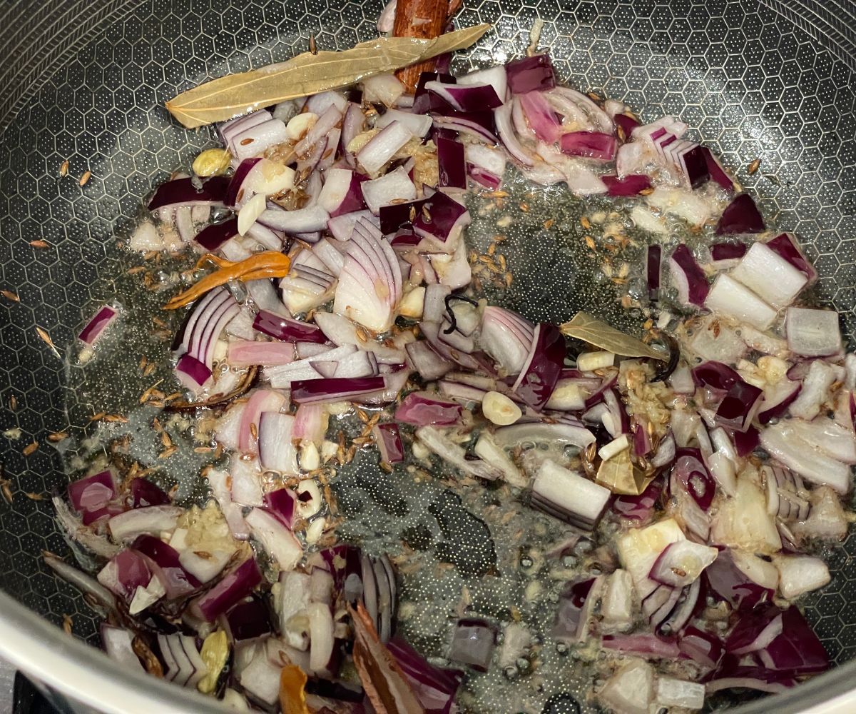 A pan is with whole spices and chopped onions over the heat.