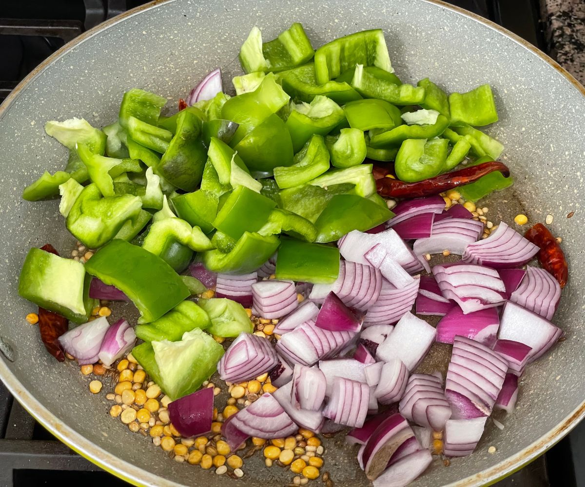 A pan is with spices, capsicum and chopped onions over the flame.