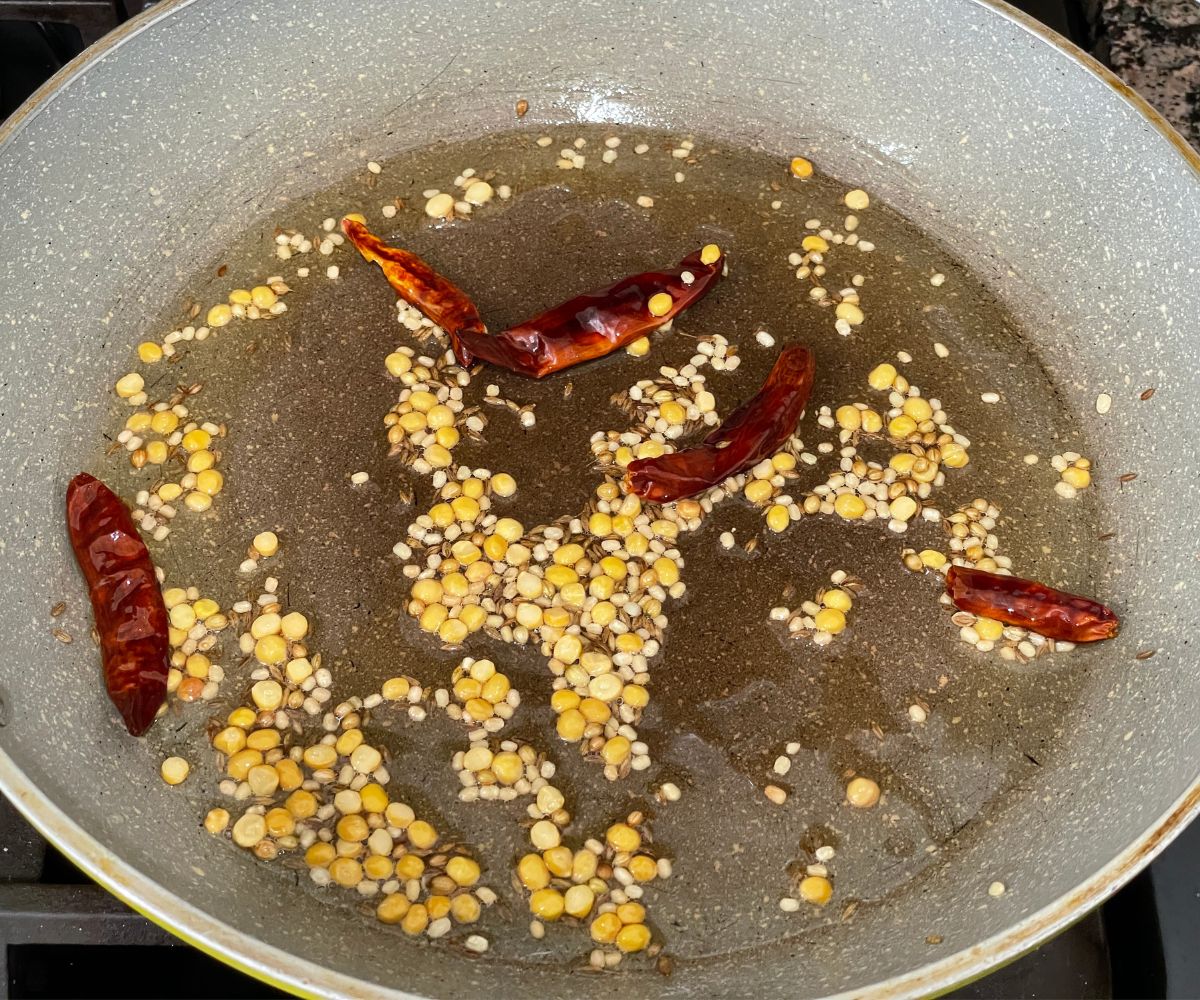 A large pan is with oil, spices and red chili over the heat.