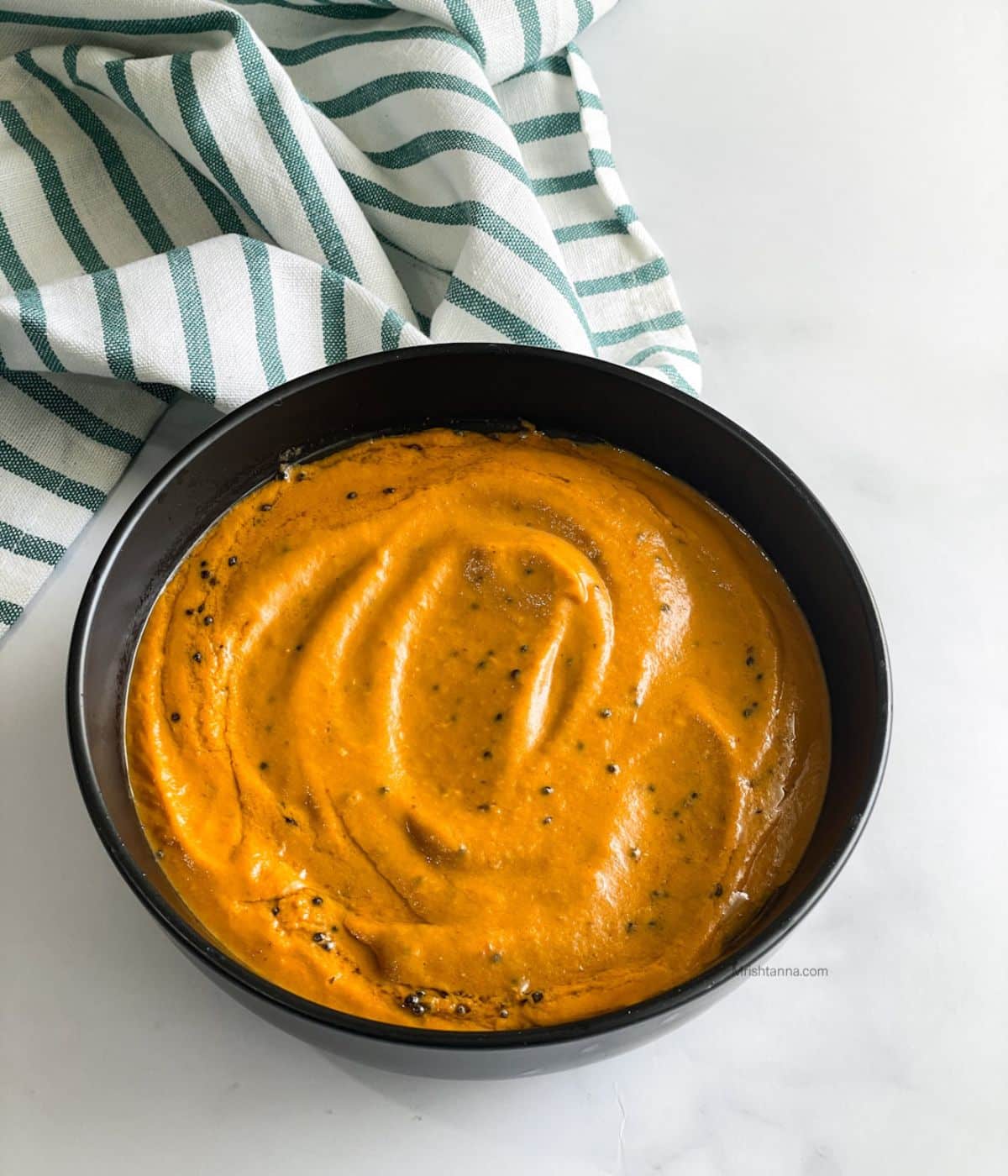 A bowl of capsicum tomato  chutney is on the table.