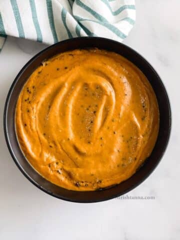 A bowl of capsicum chutney is on the table with cloth napkin by the side.