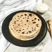 A plate of cauliflower paratha is on the table along with yogurt on the bowl