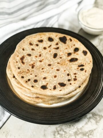 A plate of cauliflower paratha is on the table along with yogurt on the bowl