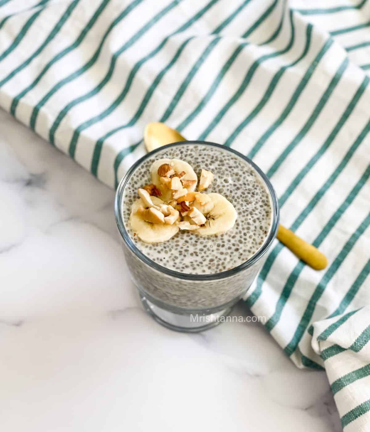 A glass of oat milk chia pudding is on the table and topped with banana.