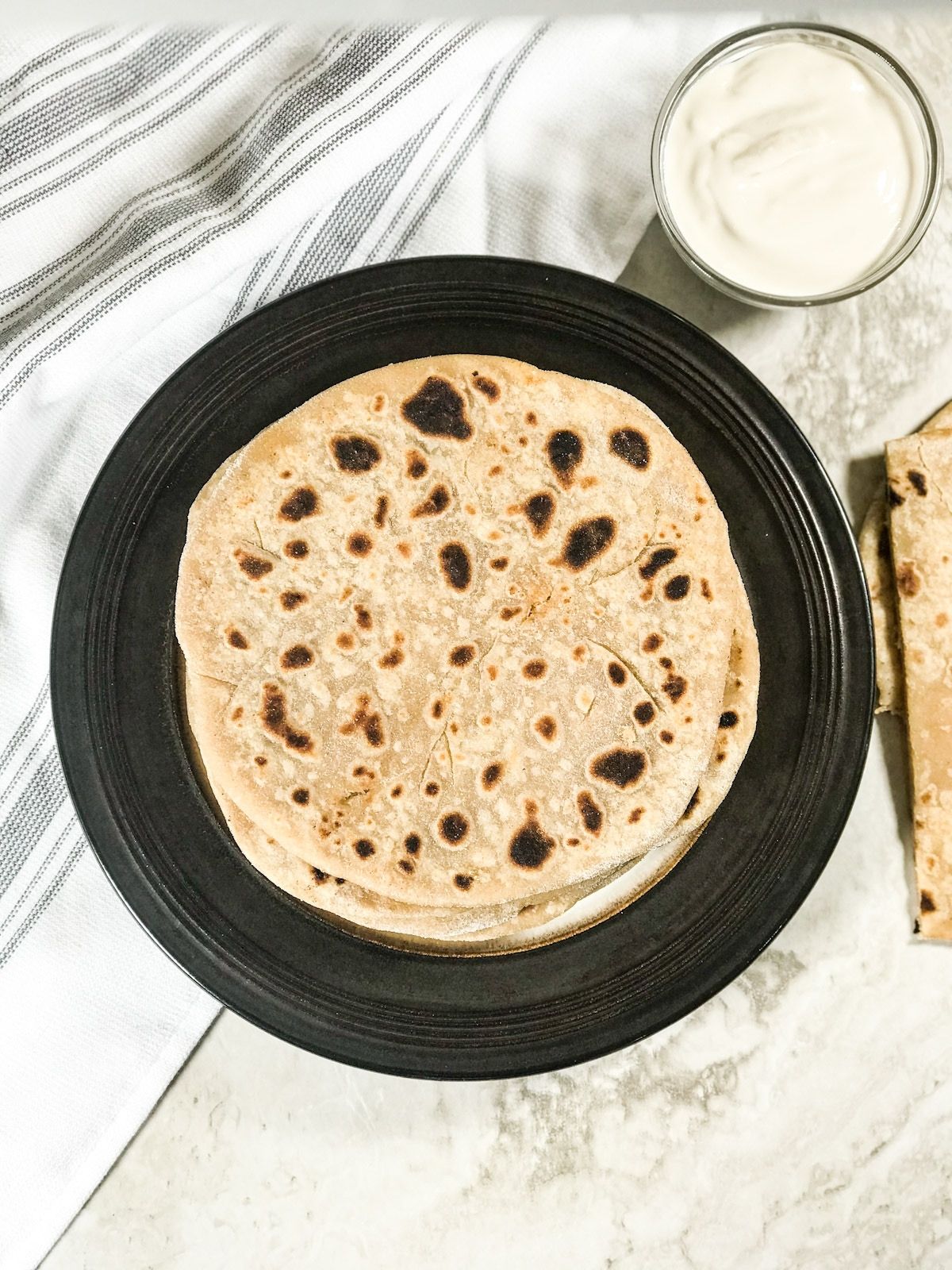 A plate of gobi paratha with side of coconut milk yogurt is on the white surface