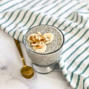 A glass of oat milk chai pudding is on the table and topped with nuts and banana.