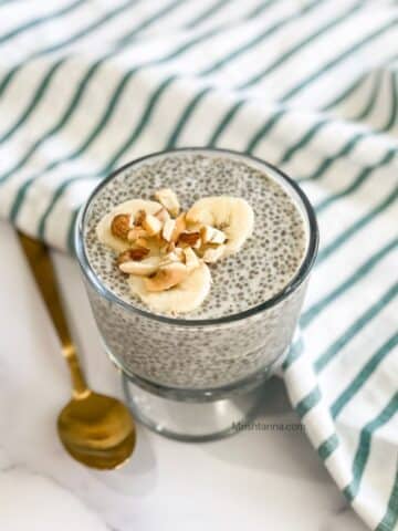 A glass of oat milk chai pudding is on the table and topped with nuts and banana.