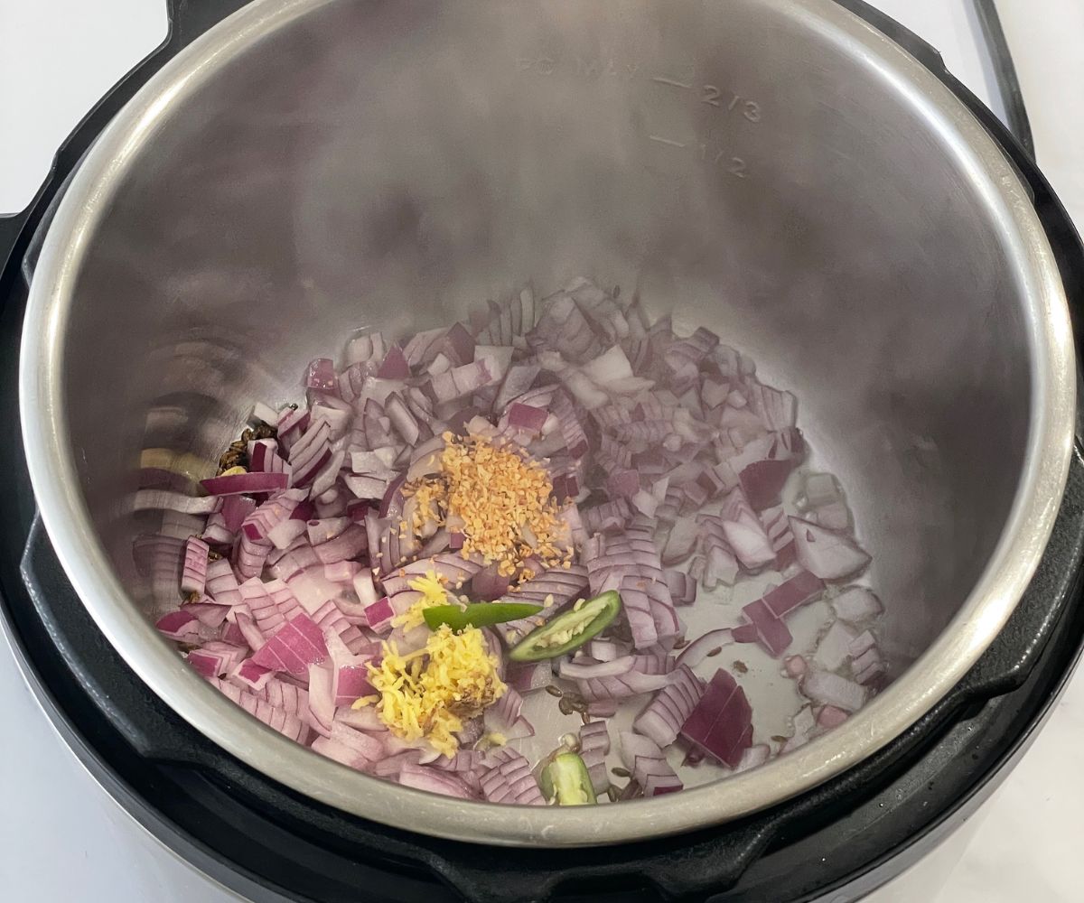 An instant pot is with oil, onions and ginger garlic on the saute mode.
