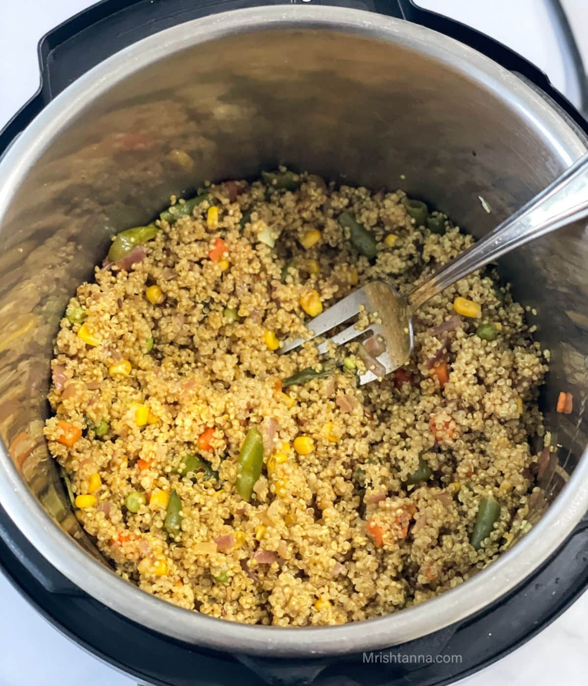 An instant pot if filled with quinoa pulao and a big fork inserted.