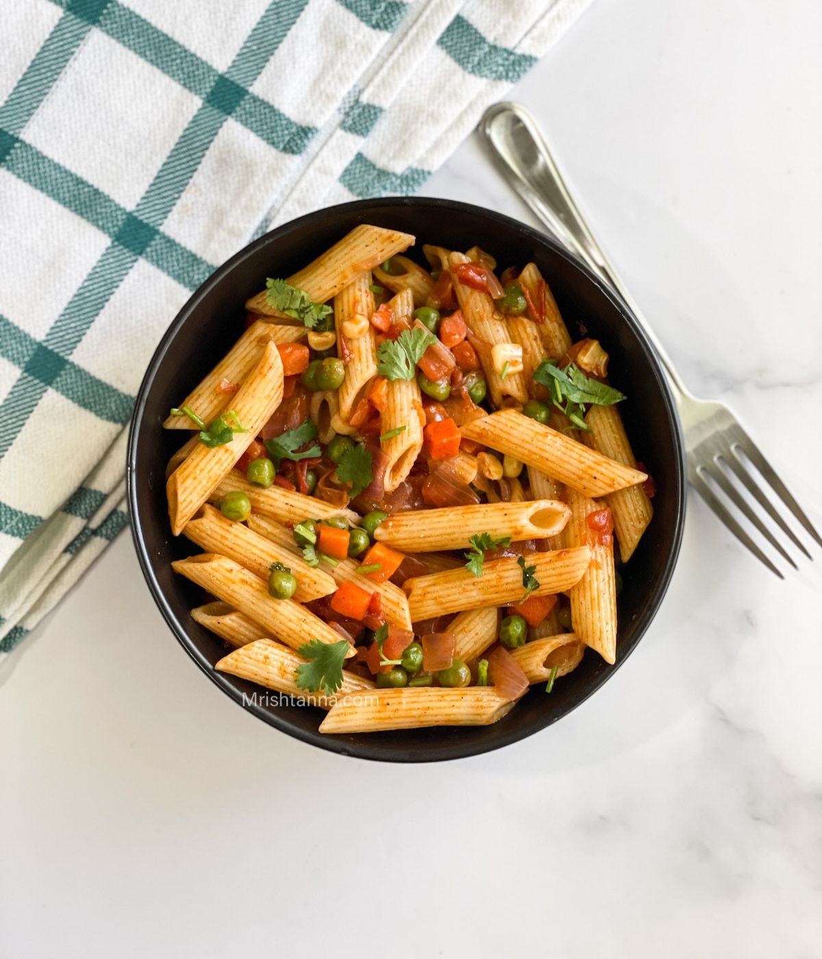 head shot of masala pasta bowl and a fork with napkin.