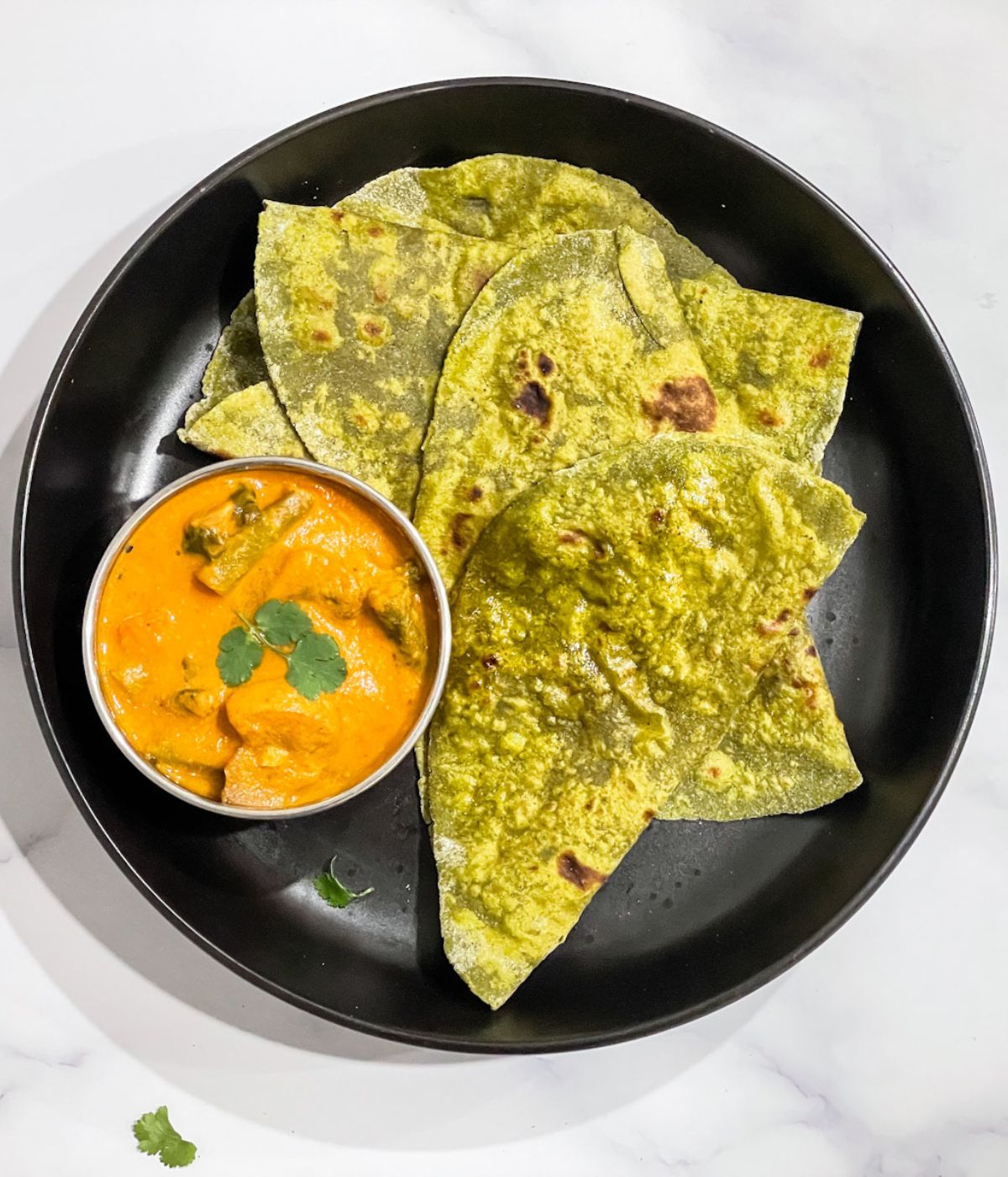 A plate of spinach paratha and curry is on the table.