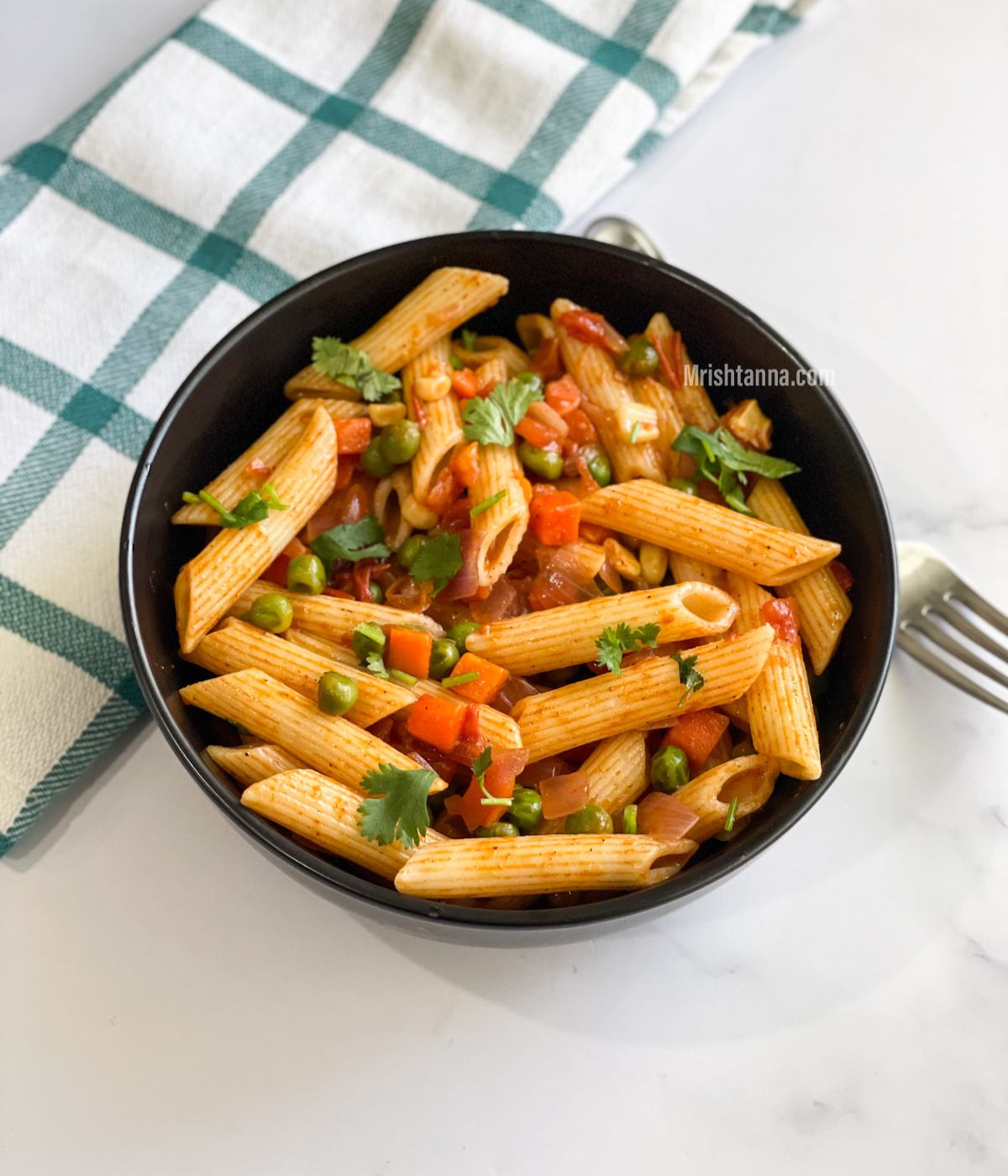 A bowl of masala pasta is on the table along with a fork.