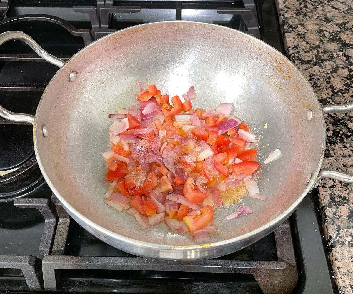 A large pan is with oil, onions and tomatoes for masala pasta.