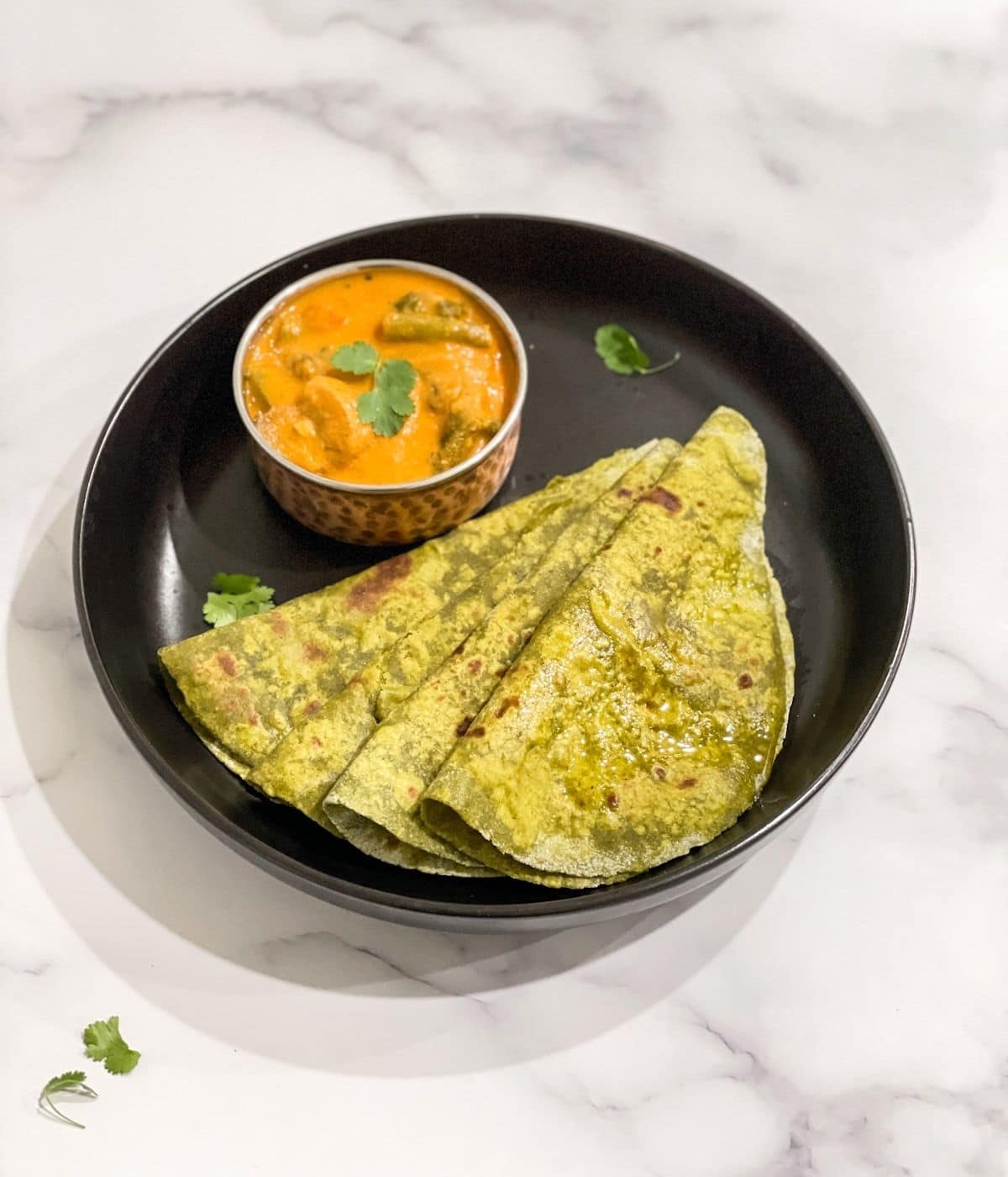 Spinach paratha is placed on the black color plate with curry.
