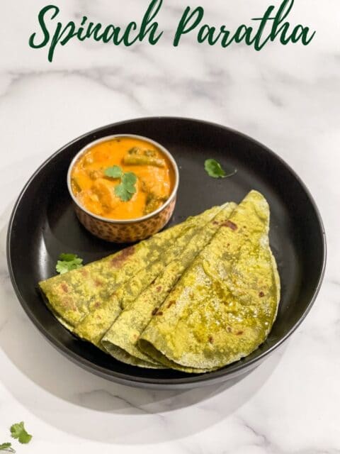 Stacks of spinach paratha is on the plate with curry.