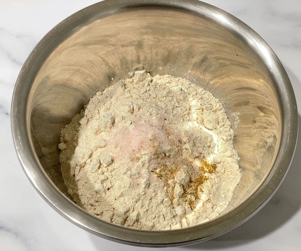 A bowl is with flour, salt and ajwain on the table.