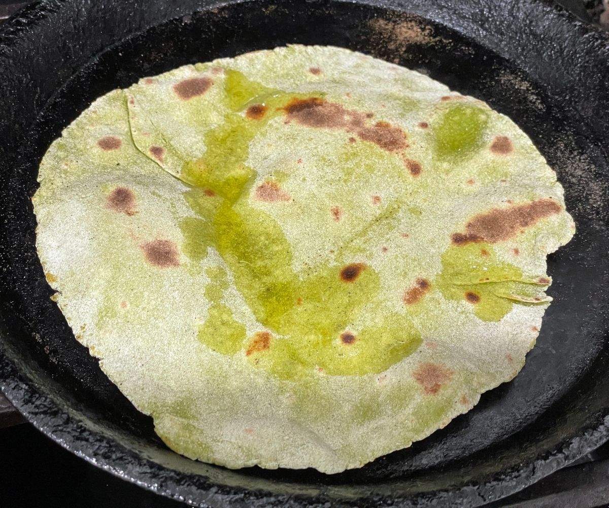 Spinach paratha is on the skillet over heat. 