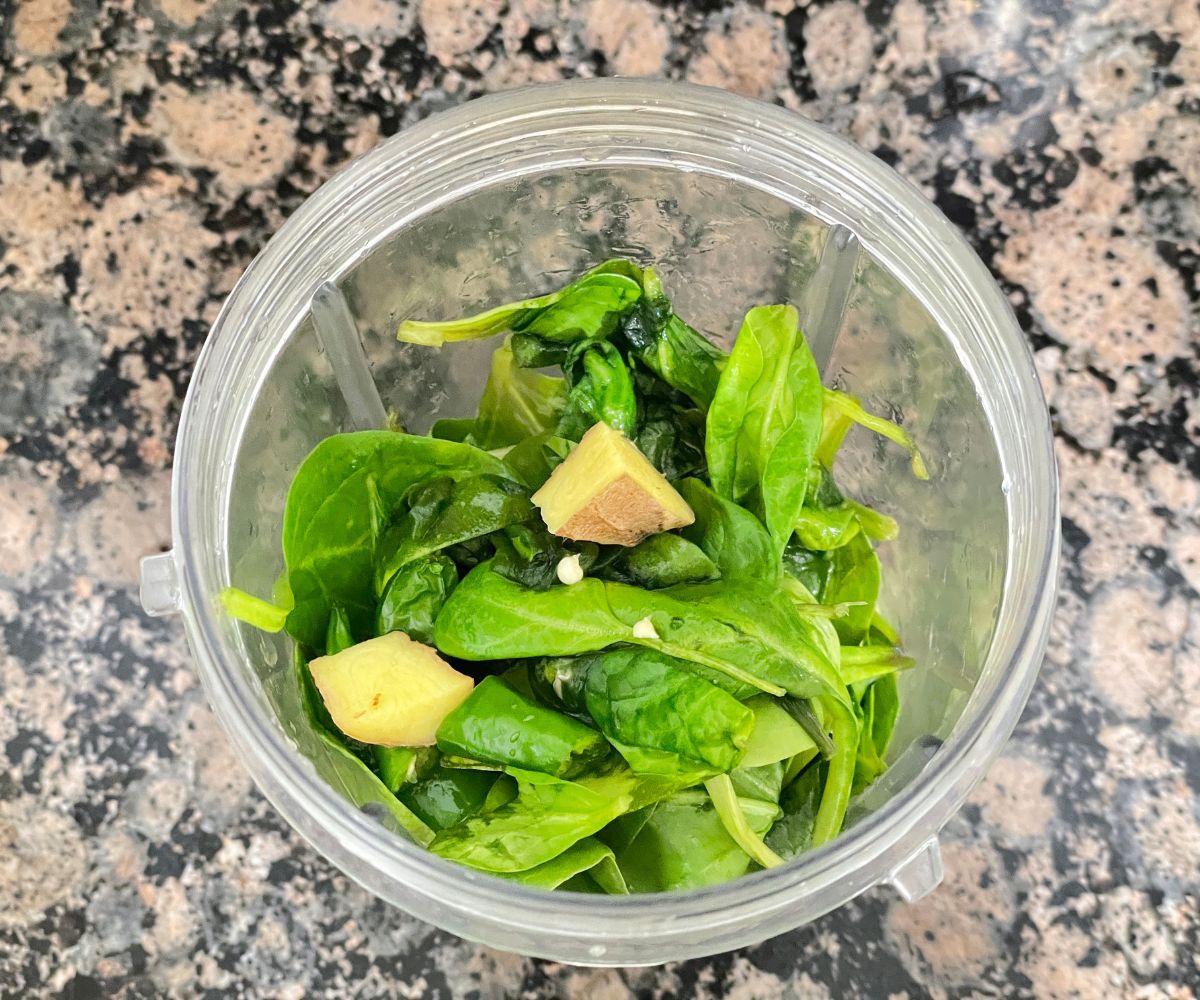 A blender is with spinach, ginger and green chili.