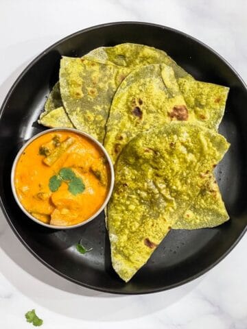 A palte is with spinach paratha's and bowl of curry.