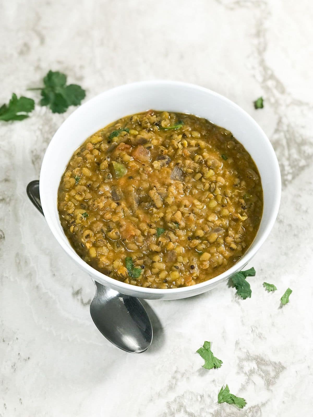 A white bowl is filled with green gram dal on the white table